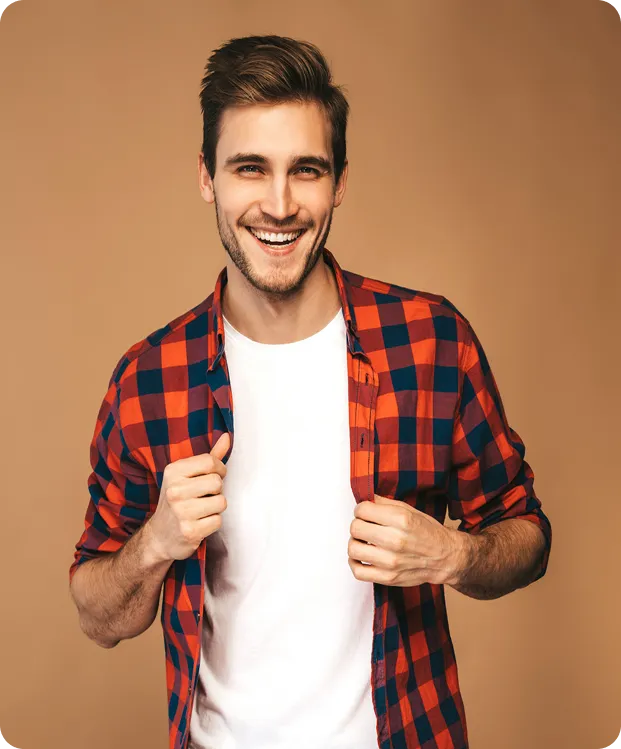 Smiling young man wearing a red and blue checkered shirt over a white t-shirt against a beige background