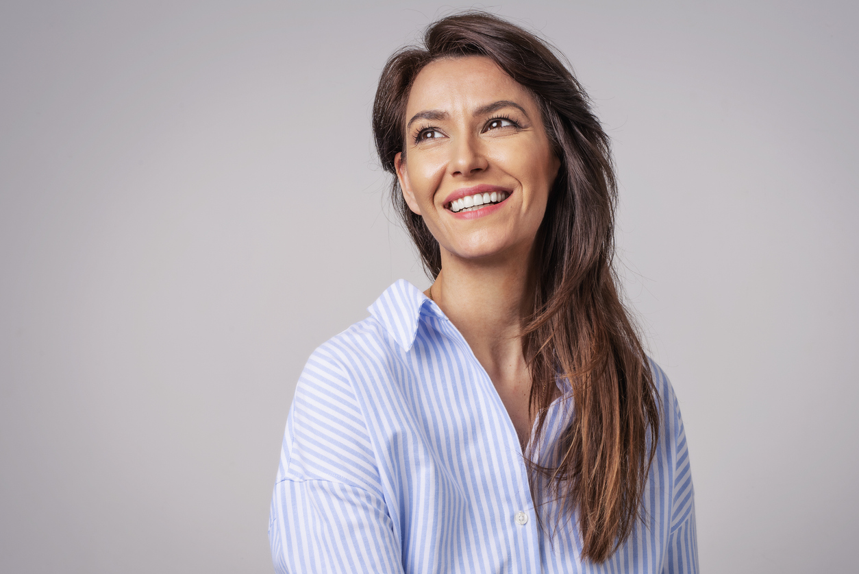 Smiling woman with long hair wearing a blue striped shirt looking away against a plain background.