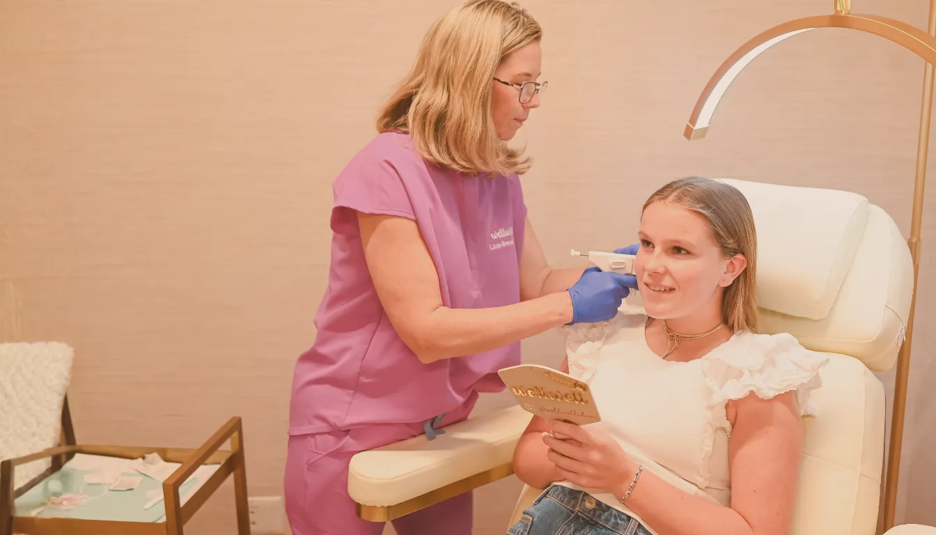 Woman in pink scrubs injecting a young woman’s cheek with a syringe in a clinic setting.