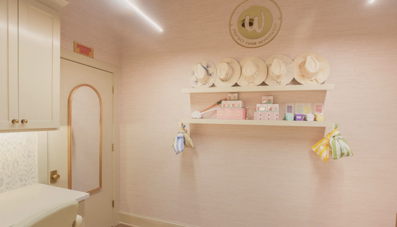 Room interior with wall shelves holding hats, beauty products, and mittens, next to a door with a mirror.