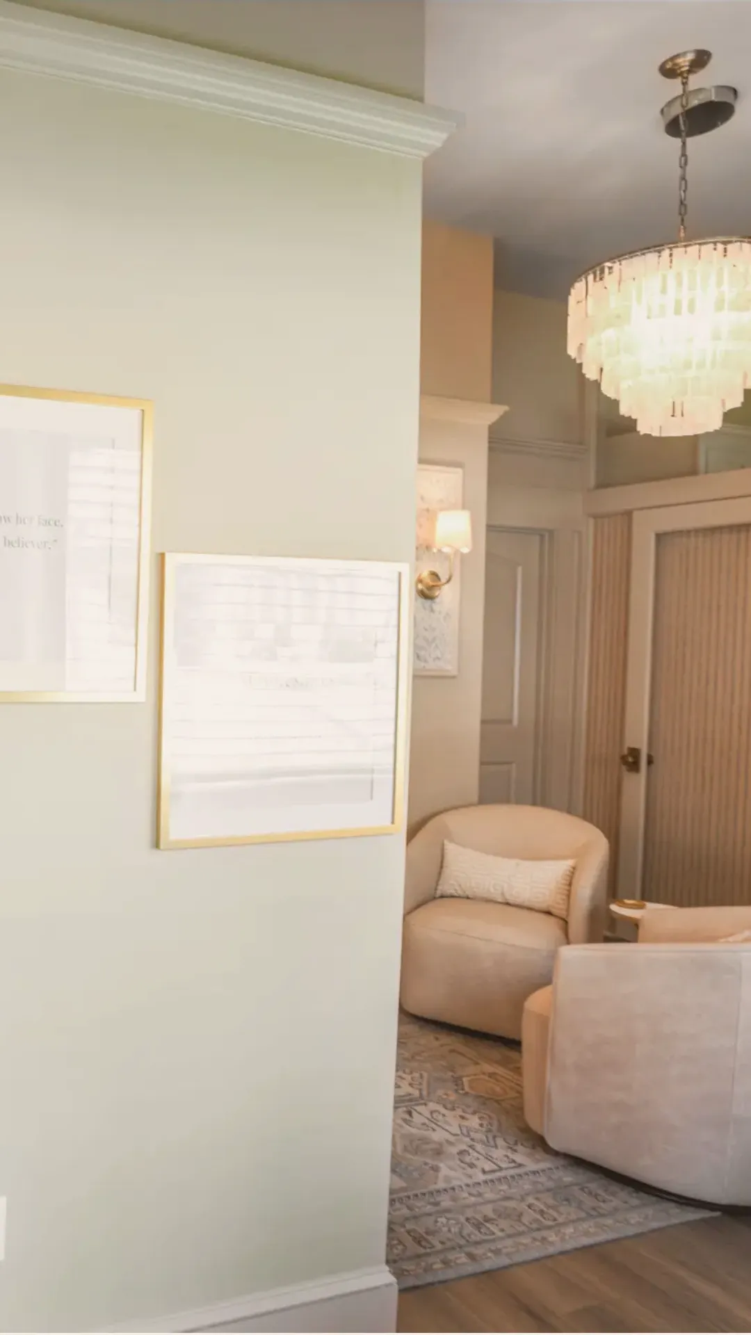Cozy corner with two beige armchairs on a patterned rug under a chandelier and wall lamp.