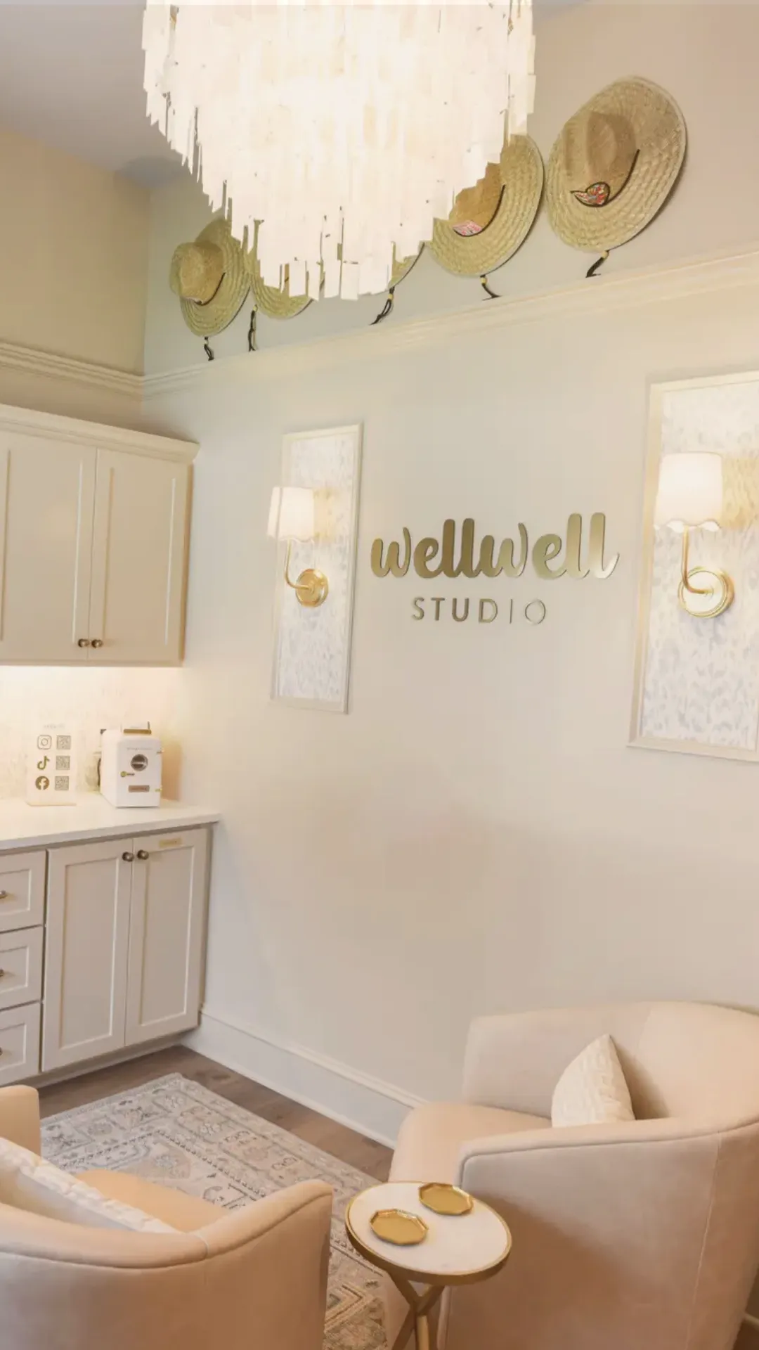 Cozy Wellwell Studio reception with beige chairs, side table, hats on wall, and soft lighting.