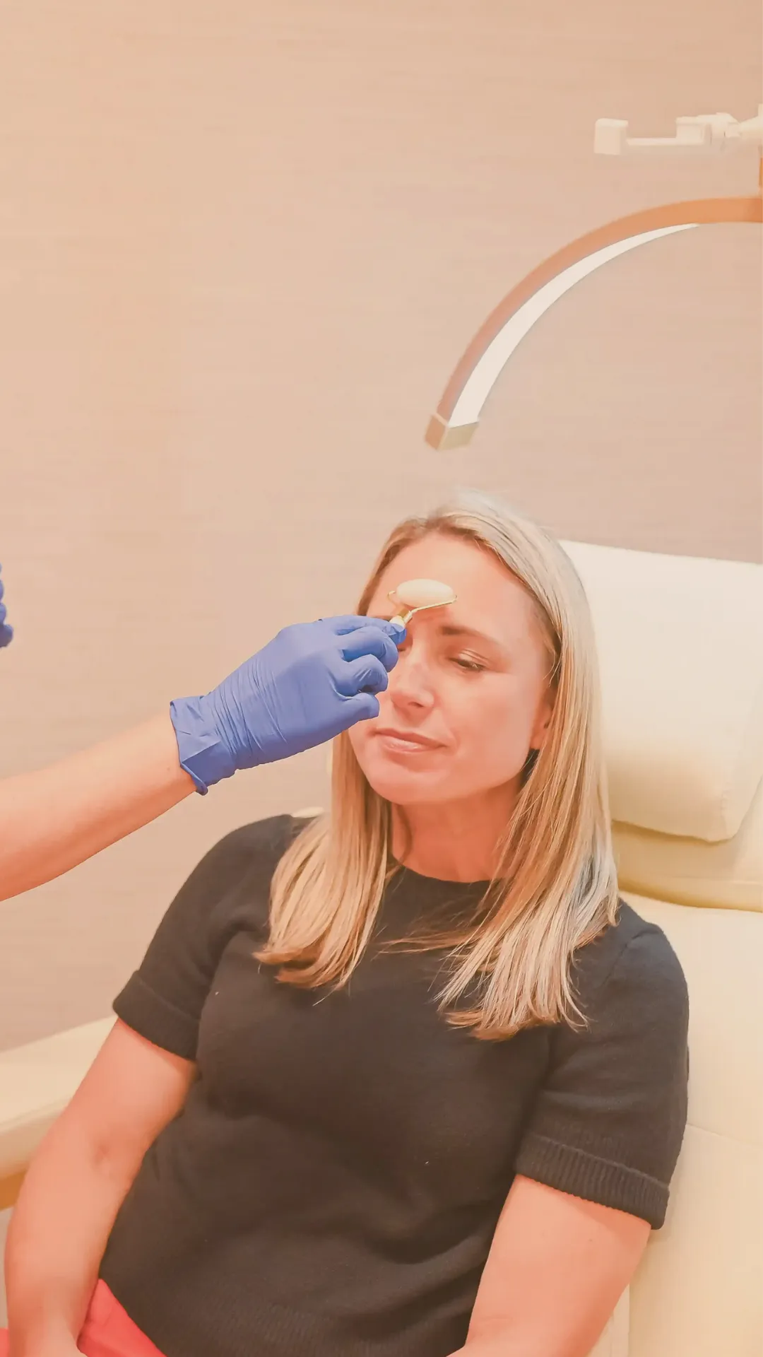 Woman with closed eyes receiving a forehead massage using a jade roller by a gloved hand.