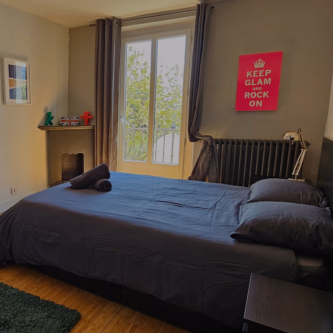 Chambre avec lit double, draps gris, fenêtre avec rideaux, tapis vert et décoration murale rose.