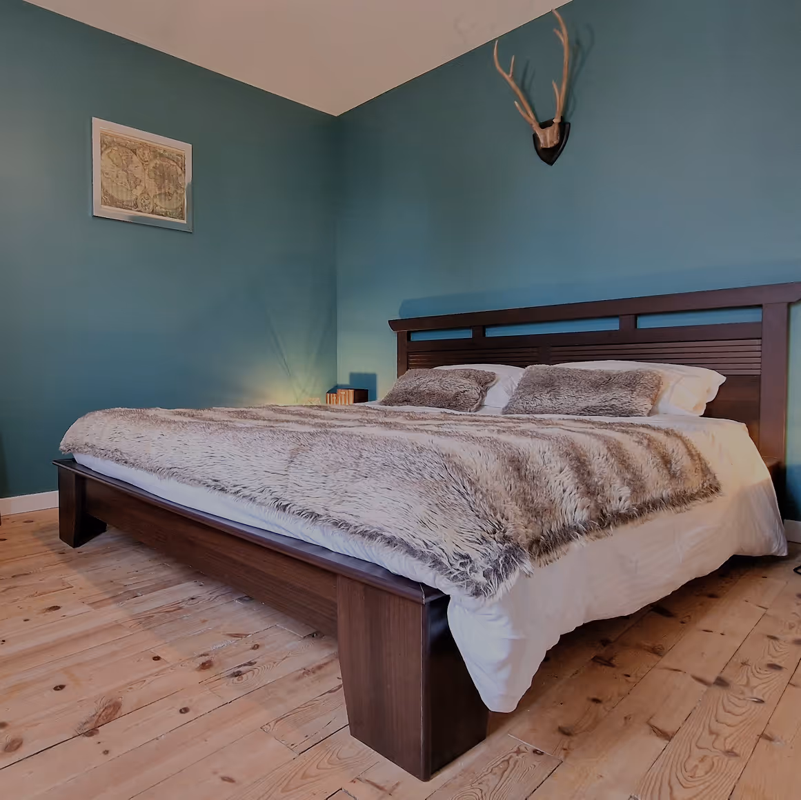 Lit double en bois avec couverture pelucheuse dans une chambre aux murs verts et sol en bois.