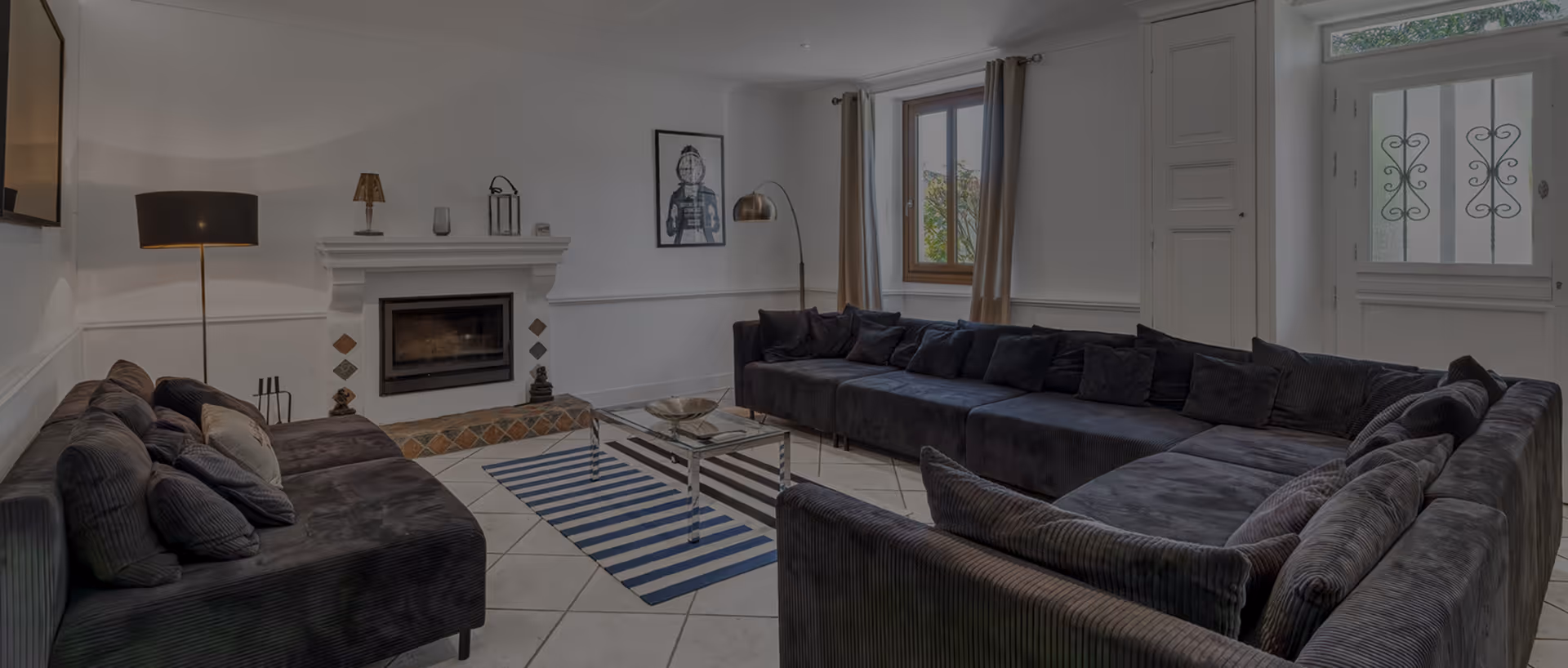 Salon moderne avec canapés gris, une cheminée, une table basse en verre, tapis rayé bleu et blanc.