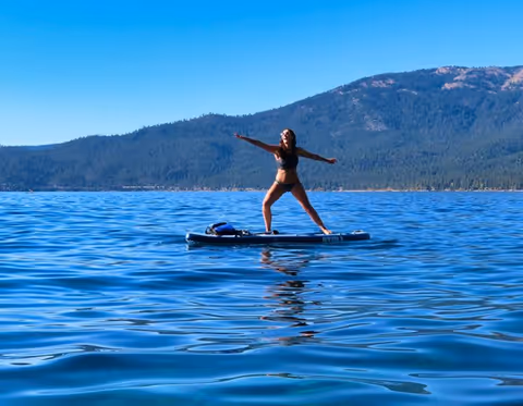 Femme faisant du yoga sur une planche de paddle sur un lac calme avec des montagnes en arrière-plan.