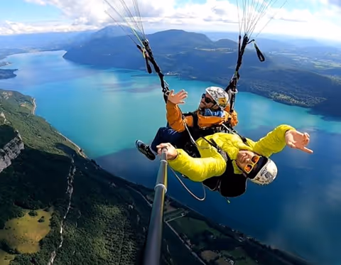 Deux personnes en parachute ascendant au-dessus d'un lac et montagnes avec ciel nuageux.