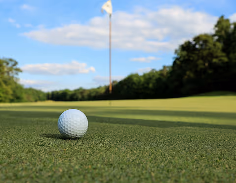 Balle de golf sur le gazon d'un green avec un drapeau de trou en arrière-plan.