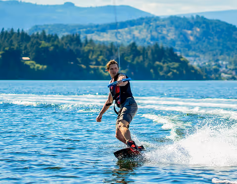 Un homme pratiquant le wakeboard sur un lac avec des montagnes en arrière-plan.