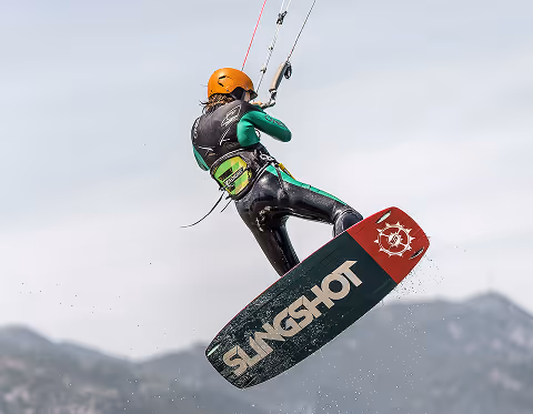 Personne en combinaison et casque orange fait du kitesurf avec une planche Slingshot en l'air.