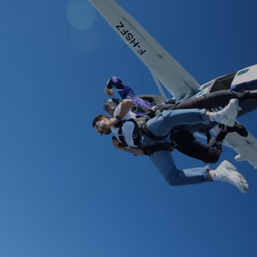Two people skydiving after jumping from a white plane under a clear blue sky.