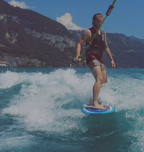 Man wakeboarding on a lake surrounded by mountains under a blue sky.