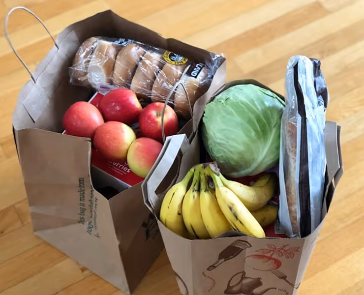 Deux sacs en papier contenant des pommes, bananes, pain, et un chou sur un sol en bois.
