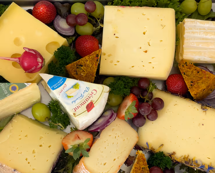 Plateau de fromages variés avec raisins, fraises, radis, oignons rouges et herbes.