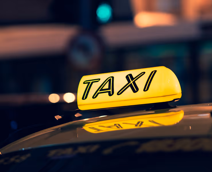 Panneau lumineux jaune TAXI sur le toit d'une voiture la nuit avec reflet sur la carrosserie.
