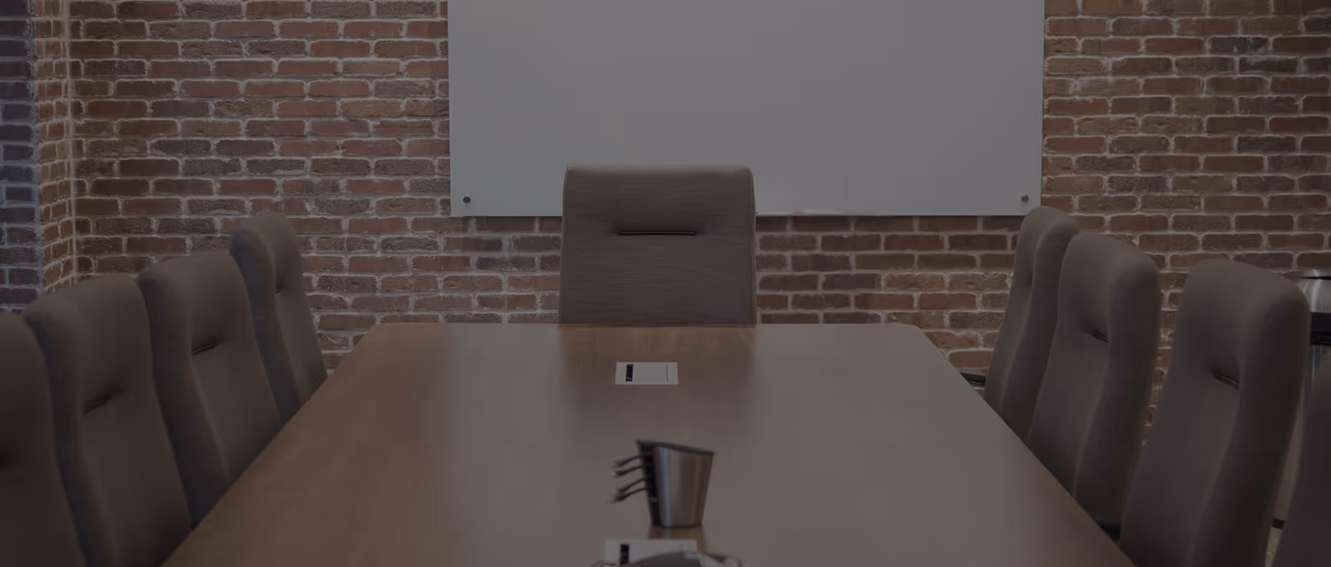 Salle de réunion avec une grande table en bois et plusieurs chaises de bureau noires.