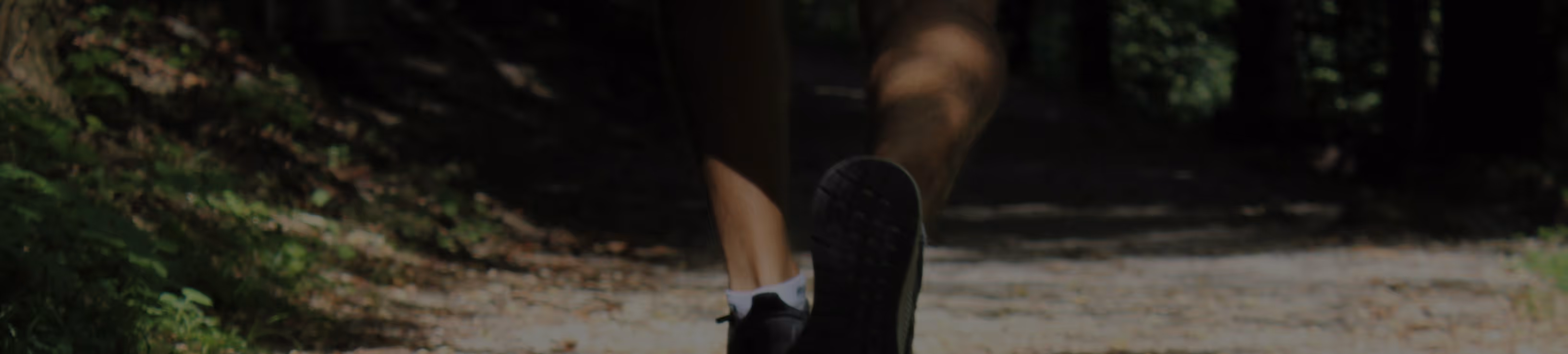 Personne courant sur un chemin en forêt avec des chaussures de sport noires.