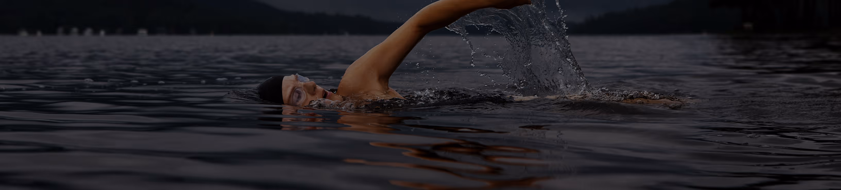 Un nageur avec un bonnet et des lunettes nage en crawl dans un lac sombre.