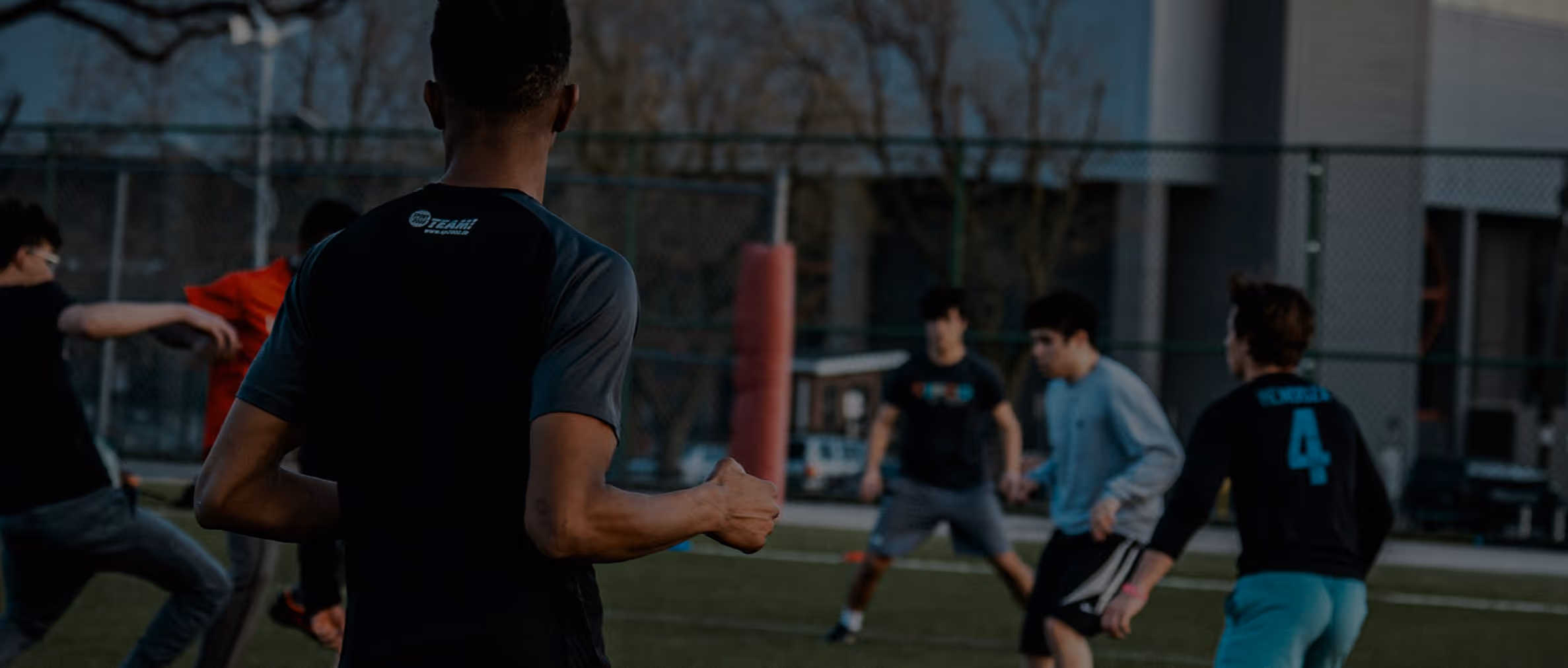Jeunes jouant au football sur un terrain extérieur en fin de journée.