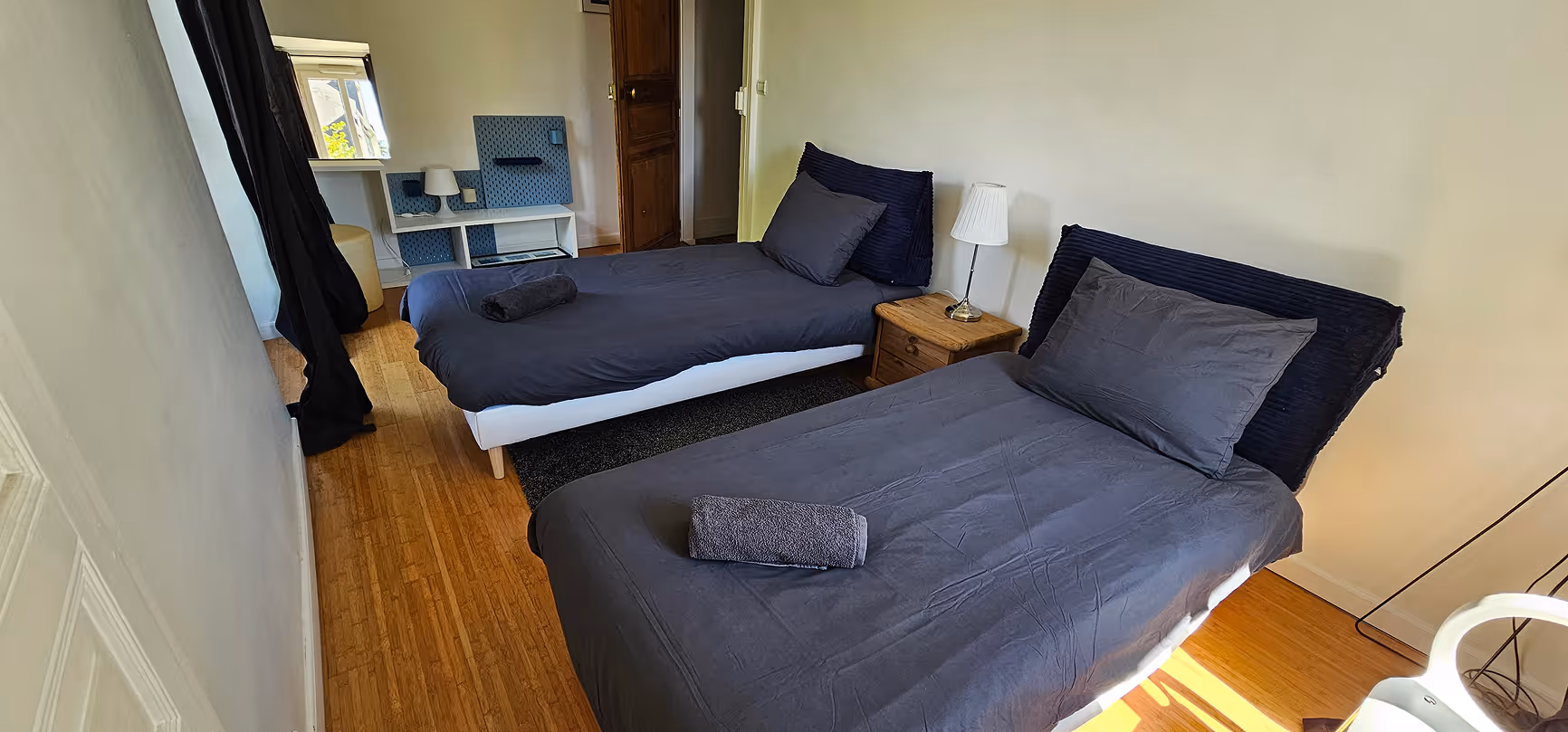 Chambre lumineuse avec grand lit, chaise, canapé, murs décorés de cadres colorés et fenêtre avec stores.