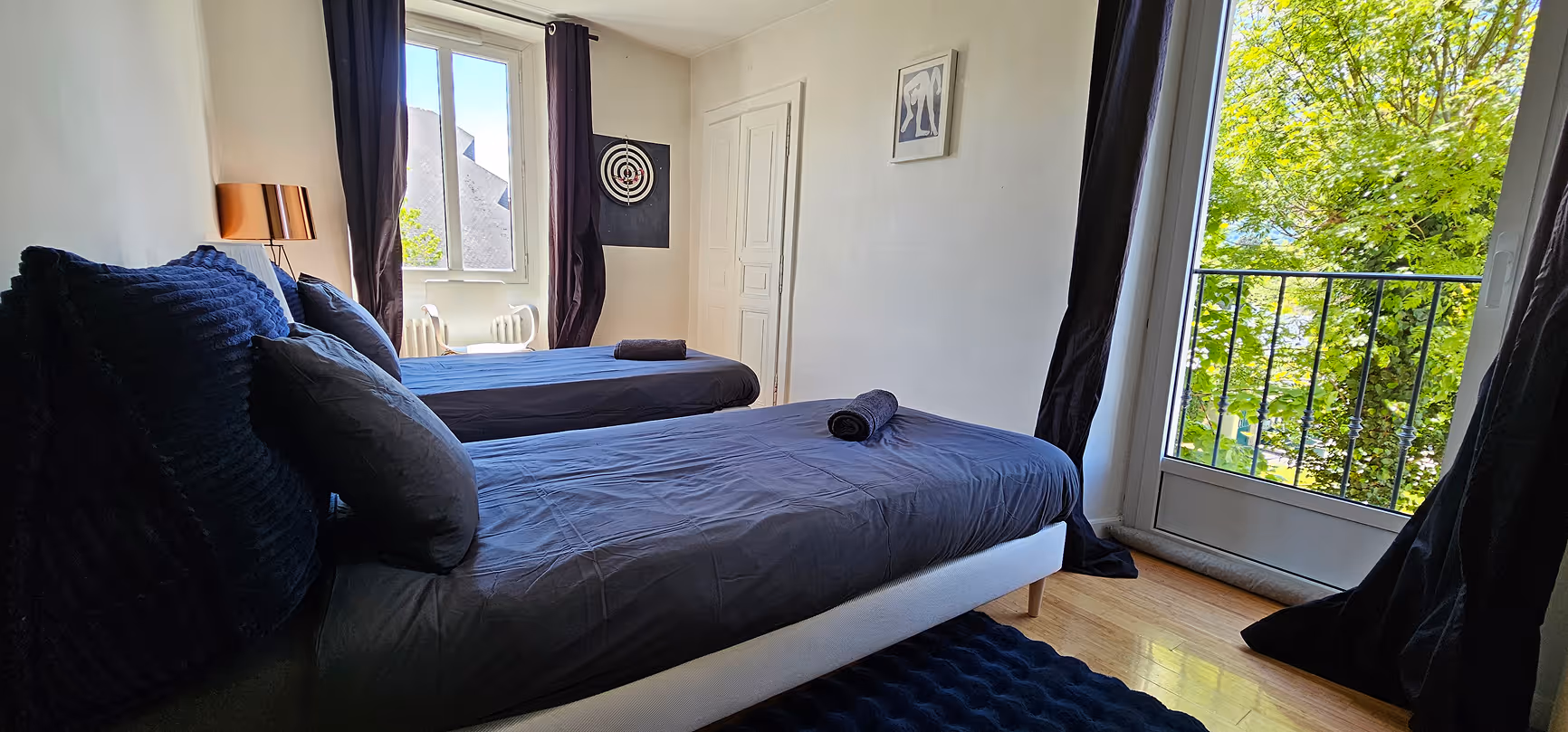 Chambre avec grand lit blanc, murs sombres, lampes murales et serviettes roulées sur le lit.