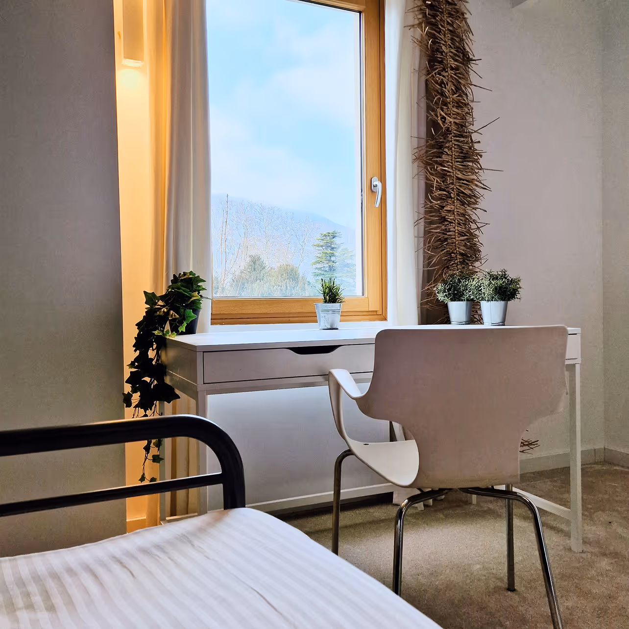 Bureau blanc près d'une fenêtre avec trois petites plantes en pot et une chaise blanche moderne.