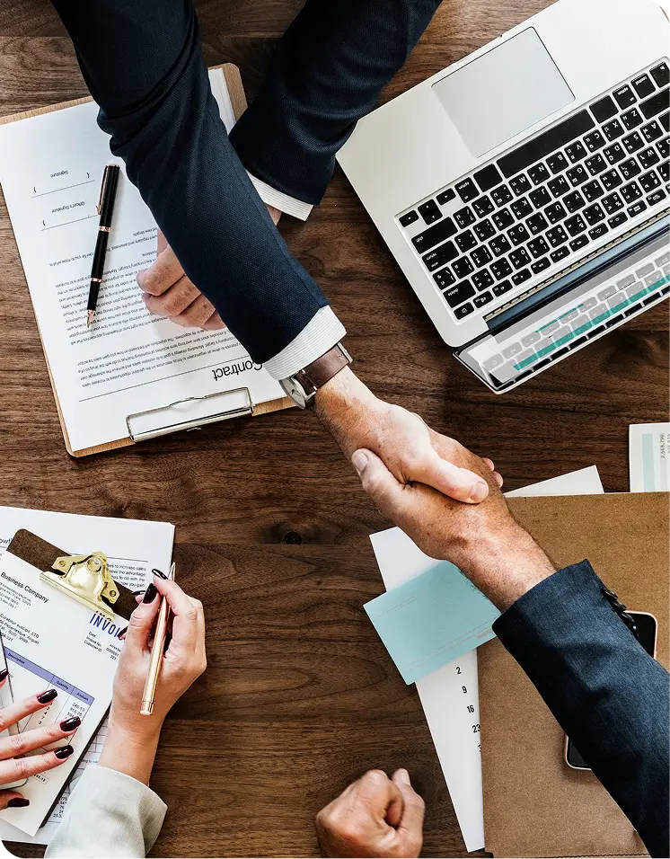 Vue de dessus de deux professionnels se serrant la main au-dessus d'un bureau avec un ordinateur portable, symbolisant le partenariat entre l'avocat et le dirigeant.