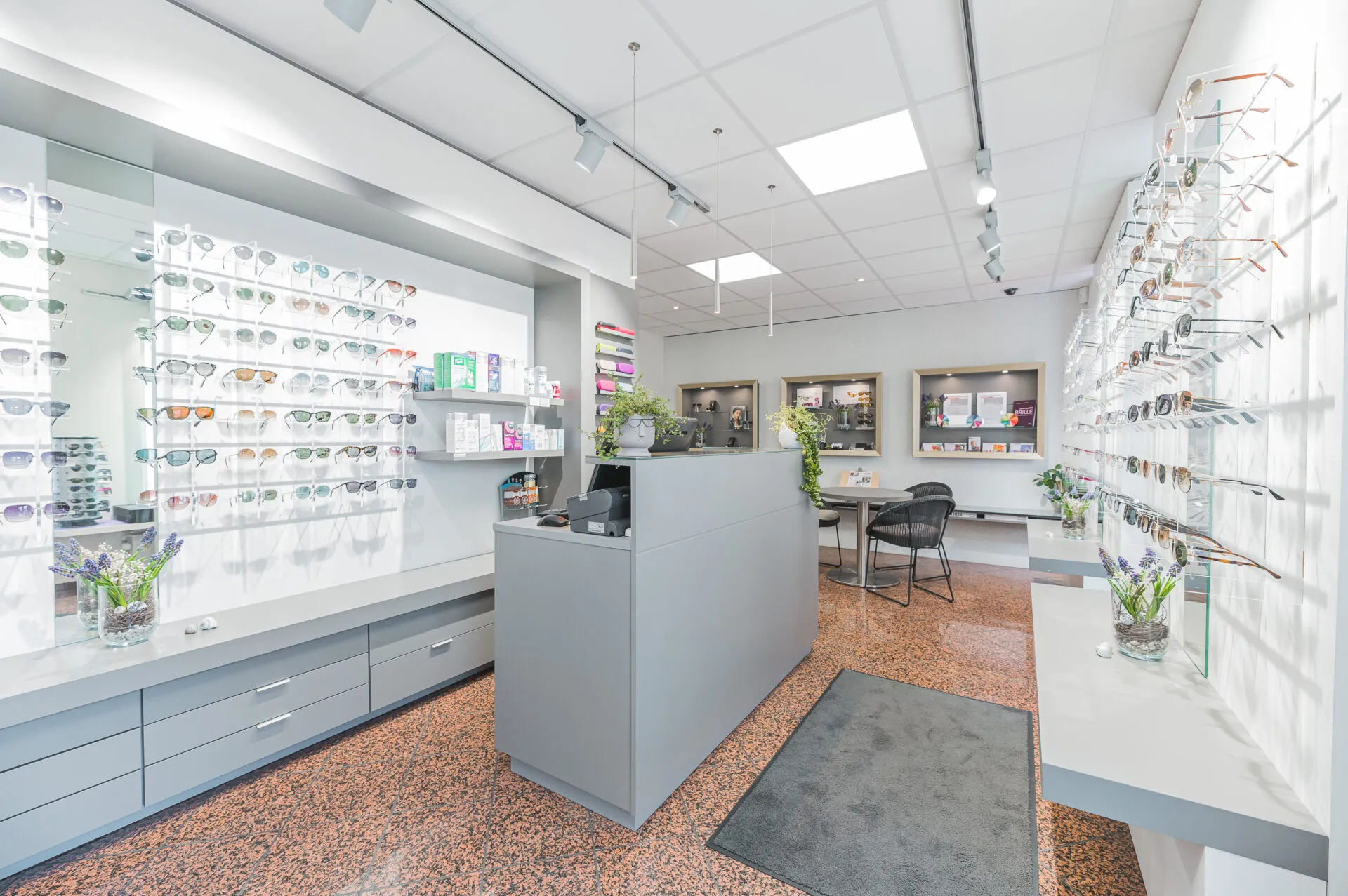 Heller Optikladen mit Sonnenbrillen an den Wänden und moderner Empfangstheke in der Mitte.