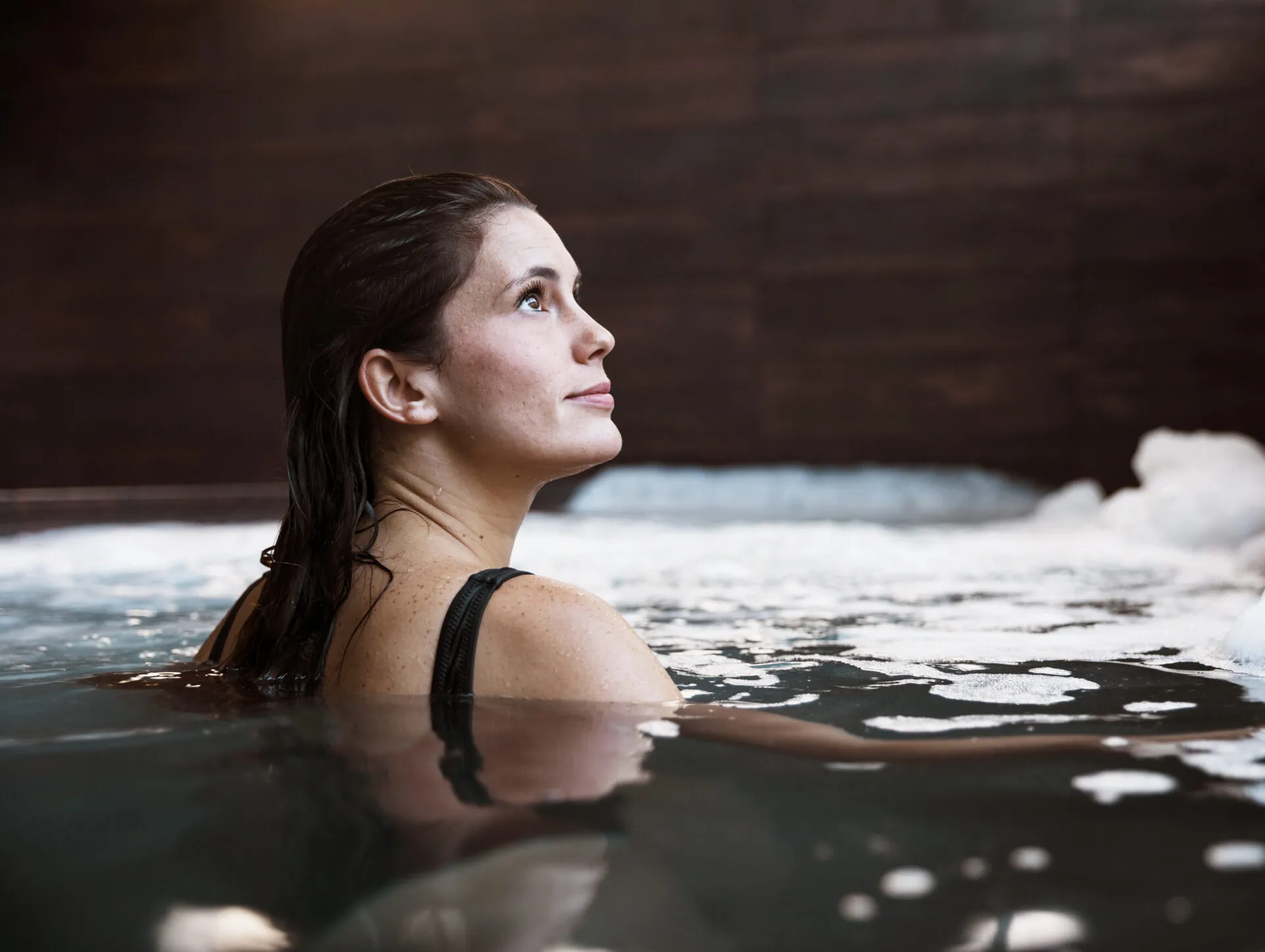 Frau entspannt im Wasser eines Spas mit dunklem Hintergrund und Schaum an der Oberfläche.