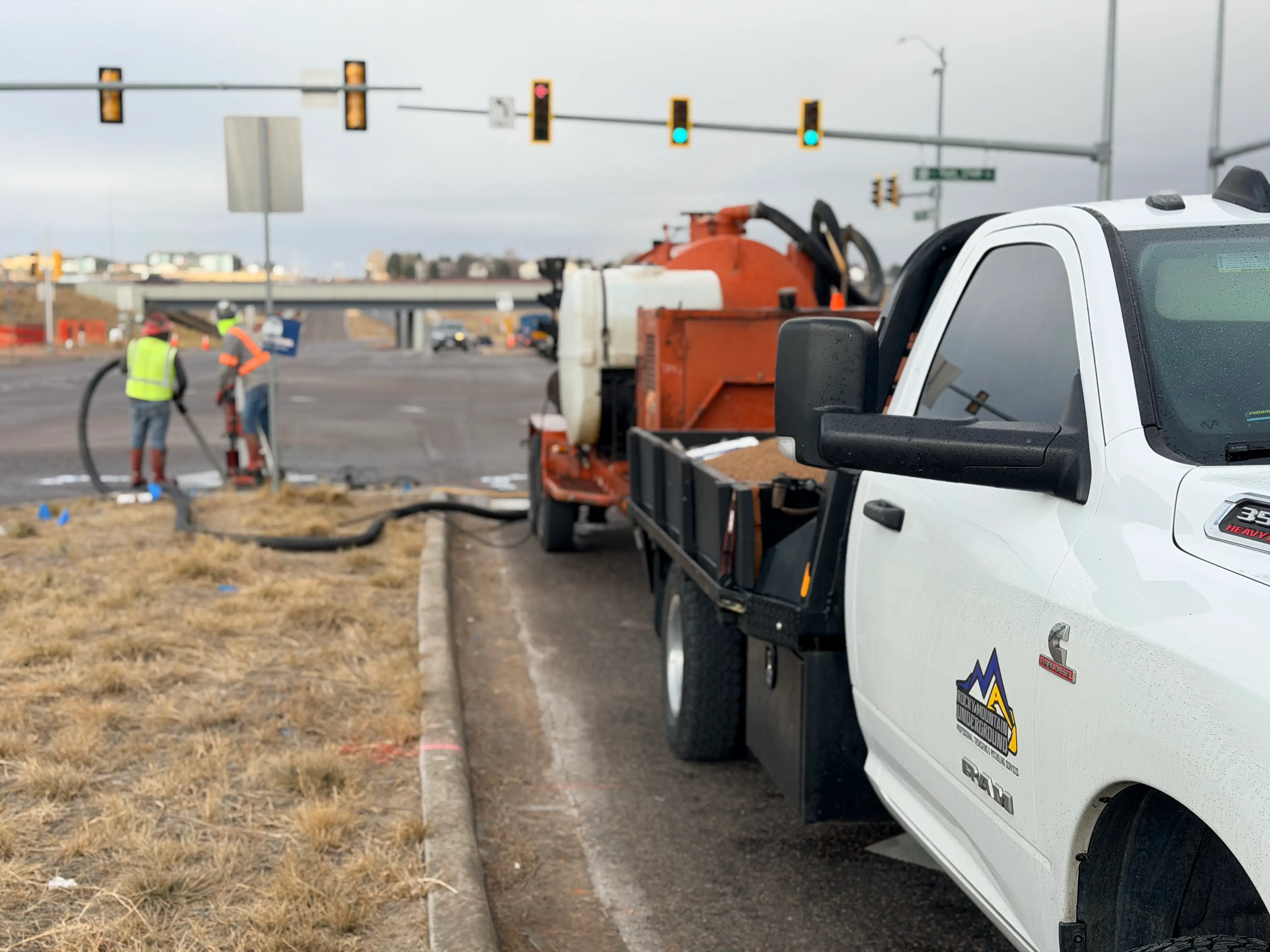 Nighttime roadwork scene with workers using machinery and cones blocking off a street near a lit Festival Center sign and a red traffic light.