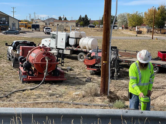 Nighttime roadwork scene with workers using machinery and cones blocking off a street near a lit Festival Center sign and a red traffic light.