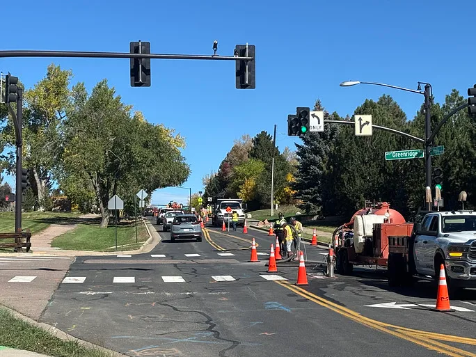 Nighttime roadwork scene with workers using machinery and cones blocking off a street near a lit Festival Center sign and a red traffic light.
