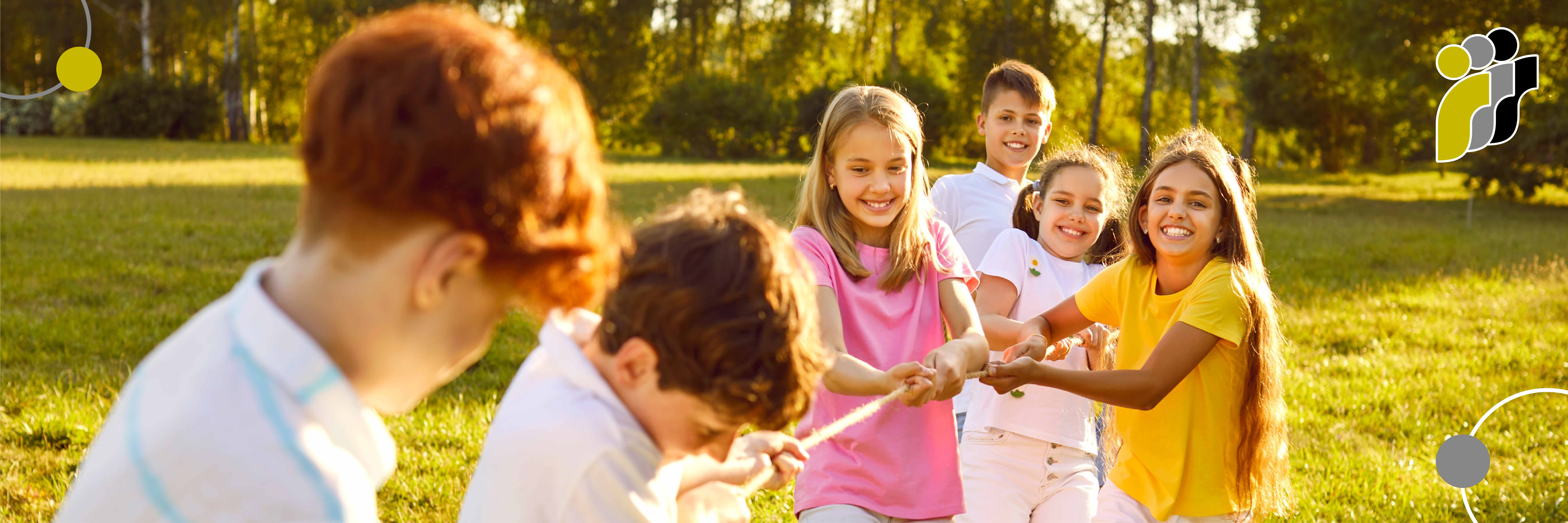 Eine Gruppe lachender Kinder spielt gemeinsam Tauziehen auf einer sonnigen Wiese.