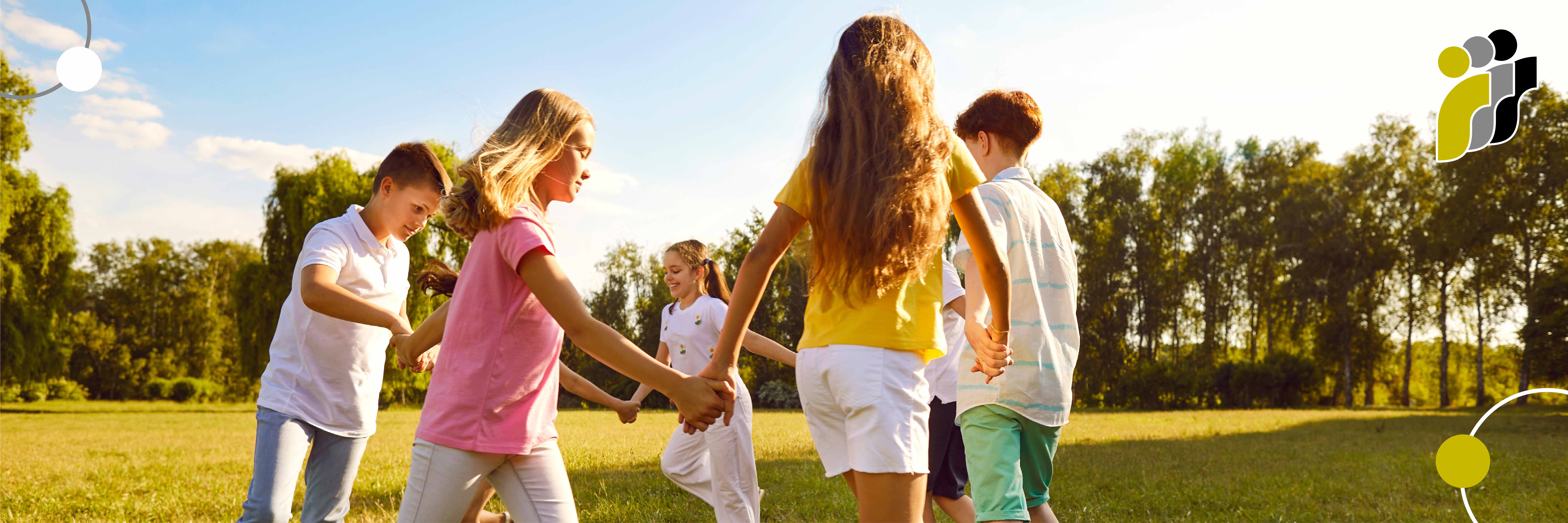 Kinder halten sich an den Händen und spielen gemeinsam auf einer Wiese im Freien bei Sonnenschein.