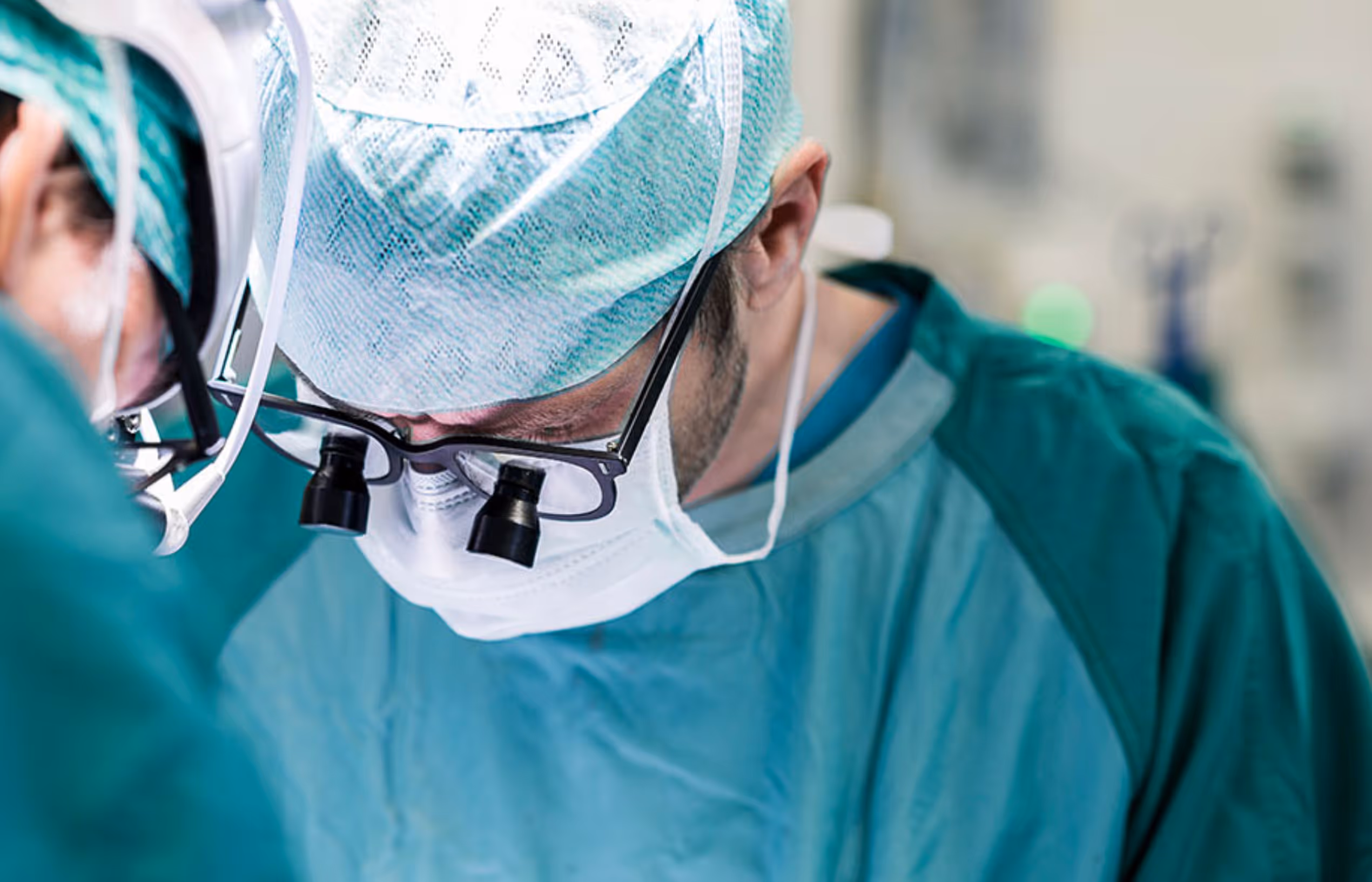 Ein Chirurg trägt OP-Kleidung, eine Haube, Maske und Lupenbrille während einer Operation.