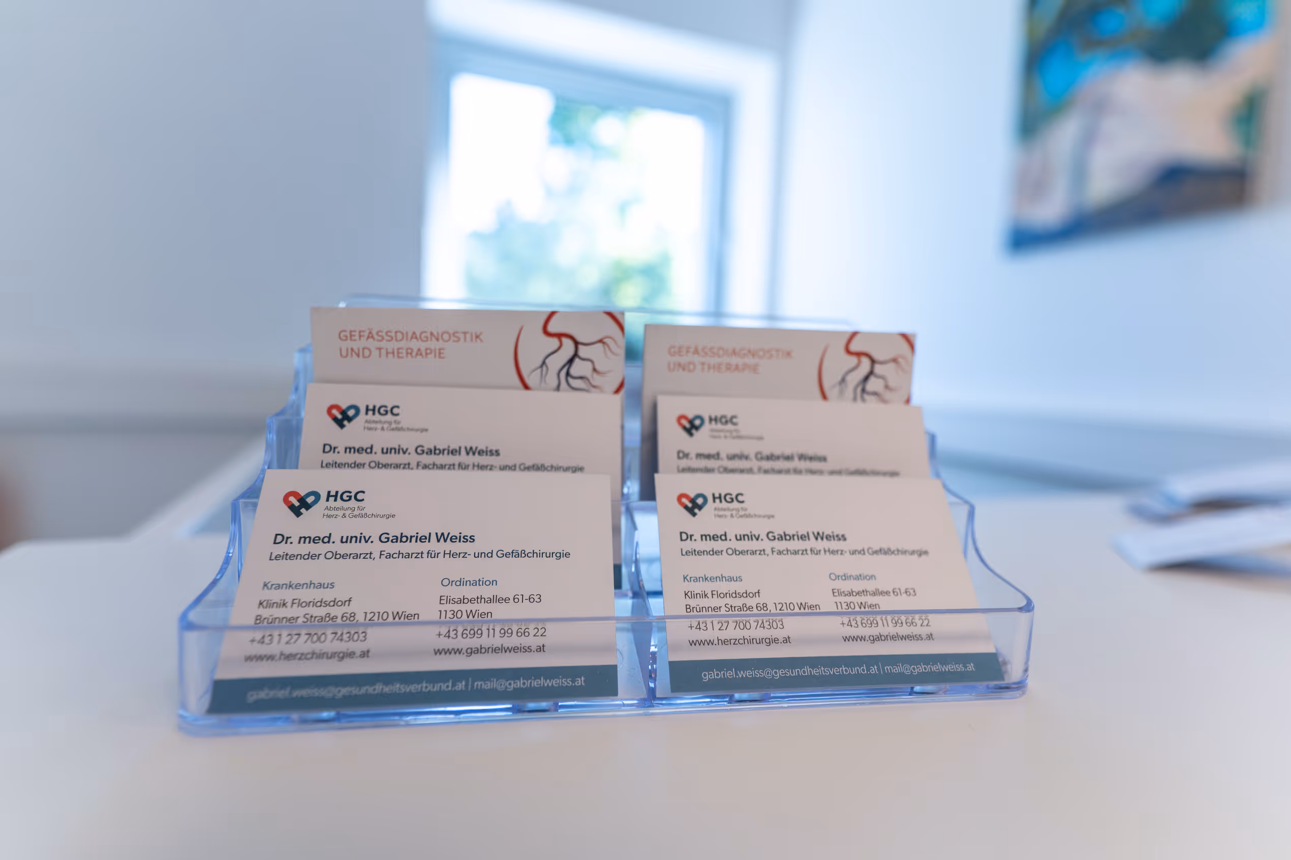 Visitenkarten von Dr. Gabriel Weiss für Herz- und Gefäßchirurgie in einem Ständer auf einem weißen Tisch.