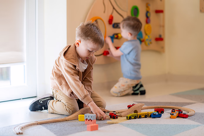 Dwóch chłopców bawi się drewnianą kolejką i zabawkami w jasnym pokoju.
