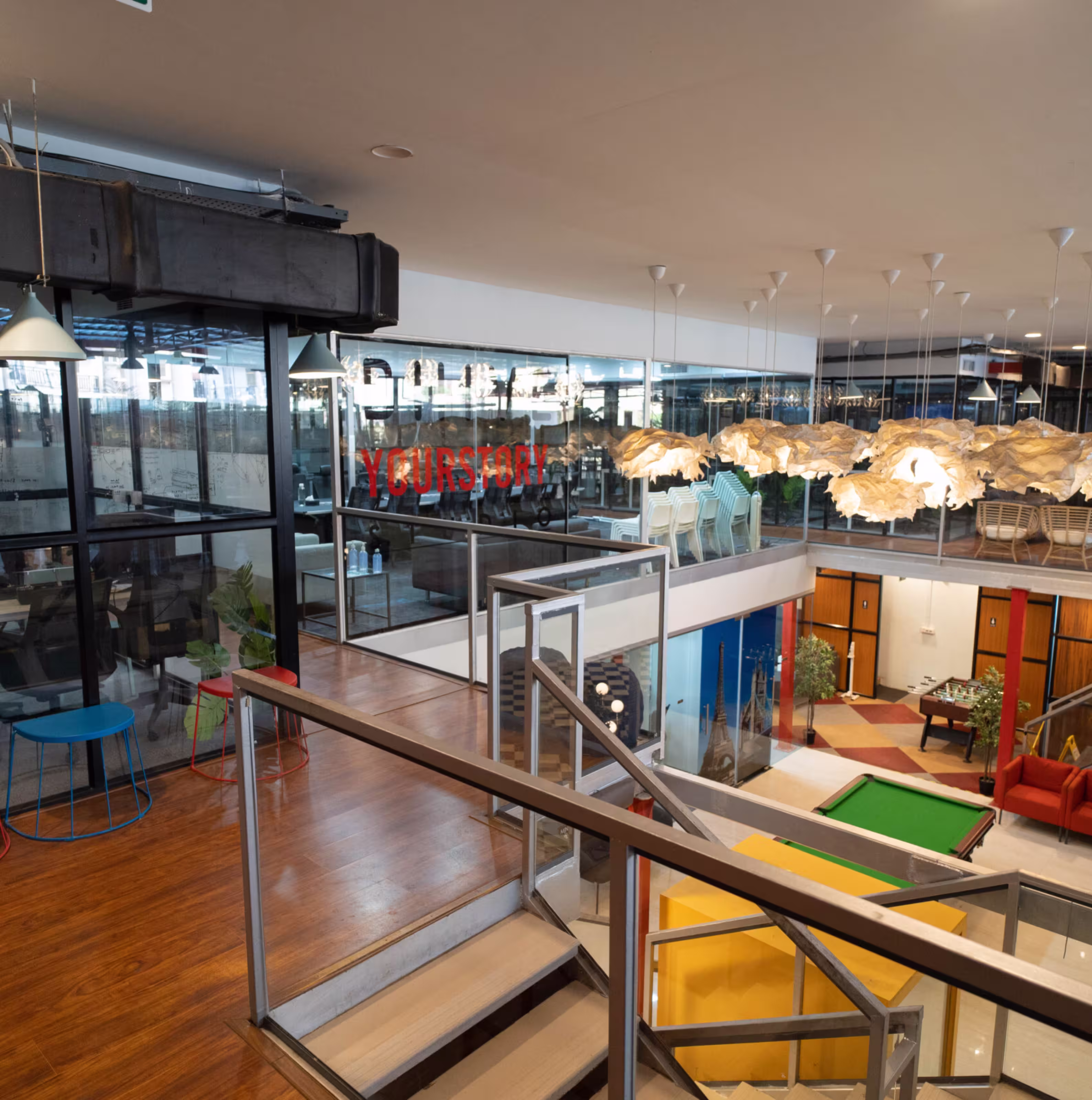 Office interior with glass walls, stairs, hanging lights, and pool table