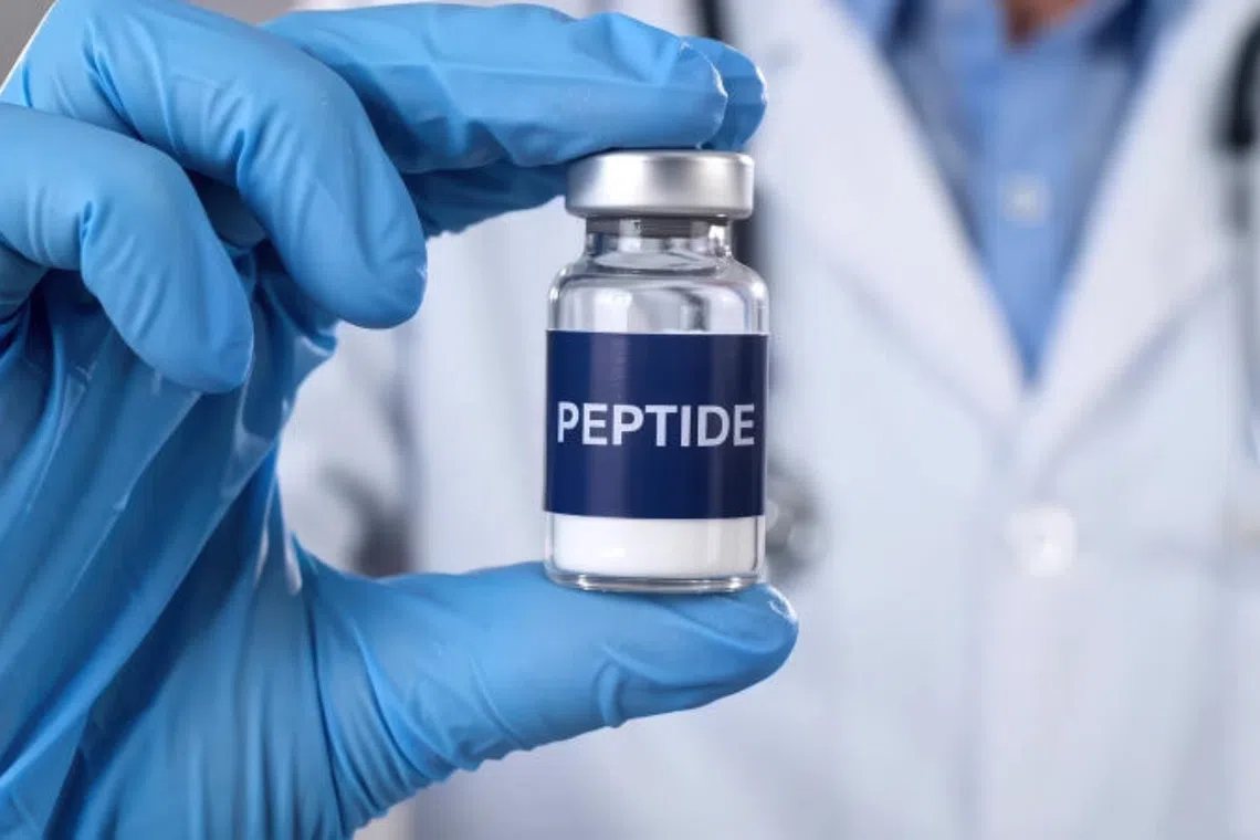 Gloved technician holding a labelled peptide vial while checking its batch number against the certificate of analysis
