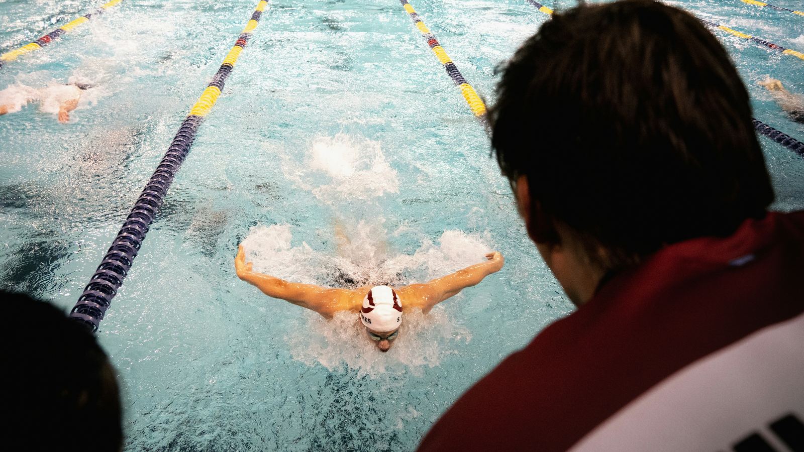 A coach on deck watching a swimmer race butterfly