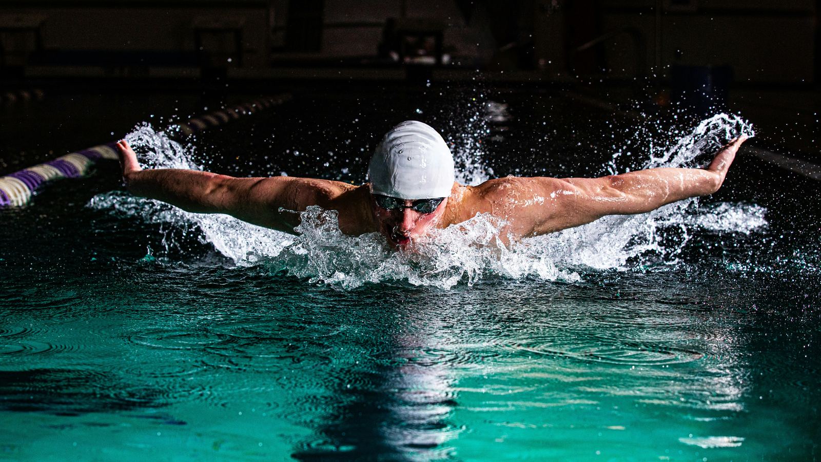 A swimmer racing butterfly in a dark indoor pool