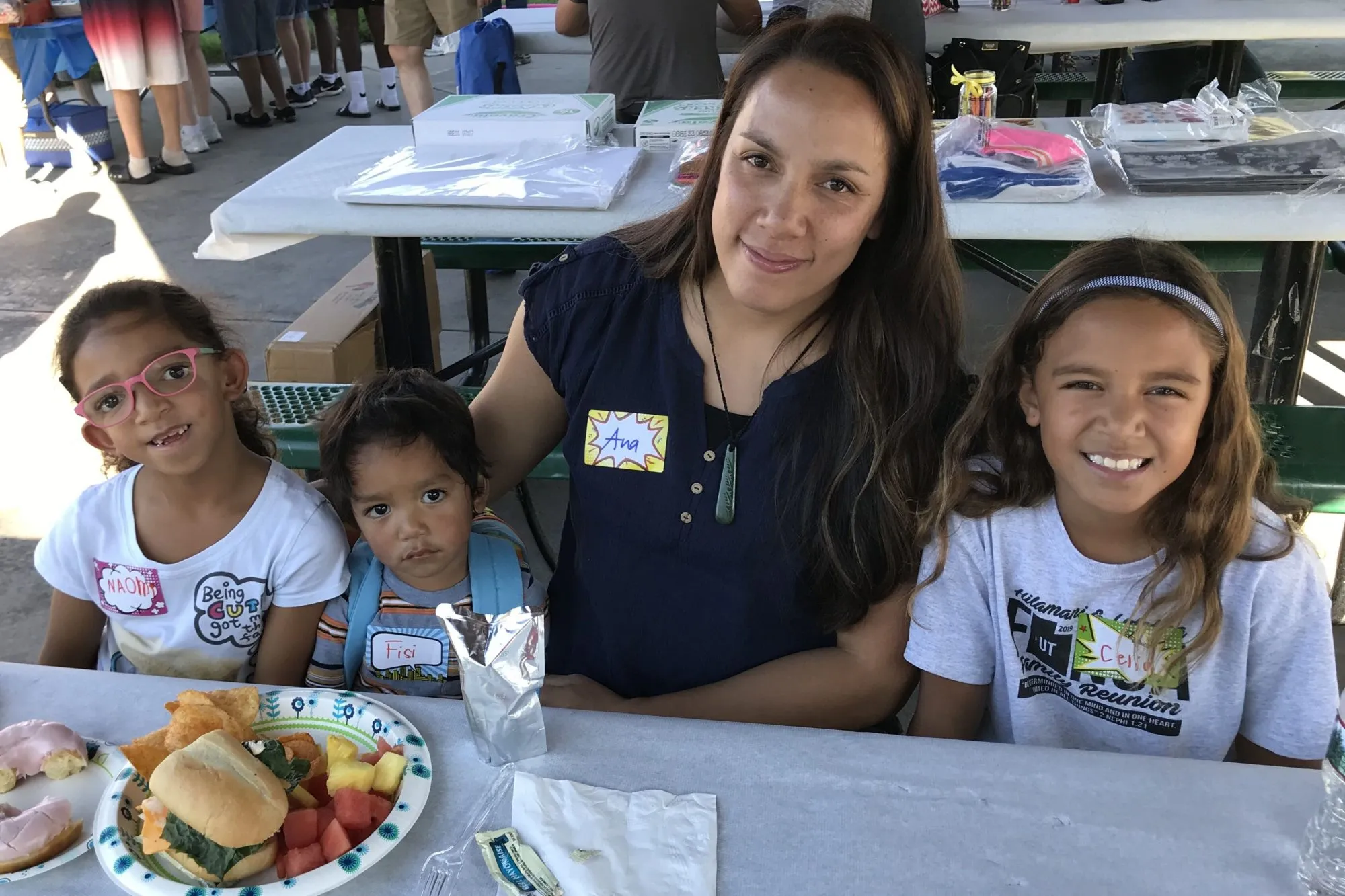 Volunteers and children smile together at a picnic table event