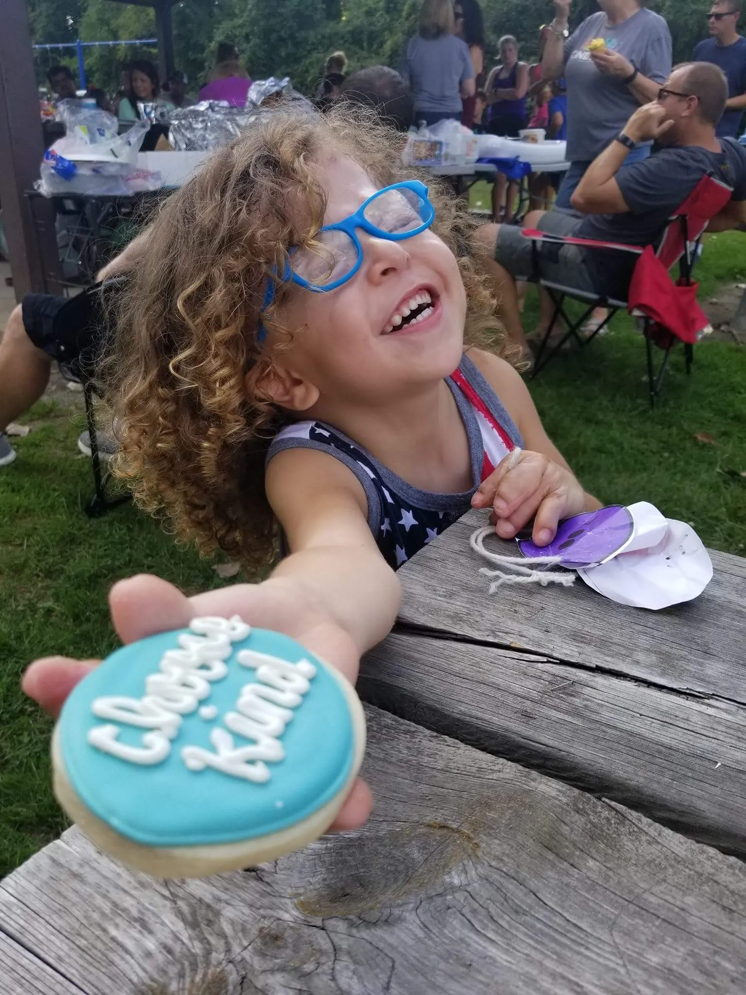 A girl smiles while holding out a cookie decorated with "Choose Kind"