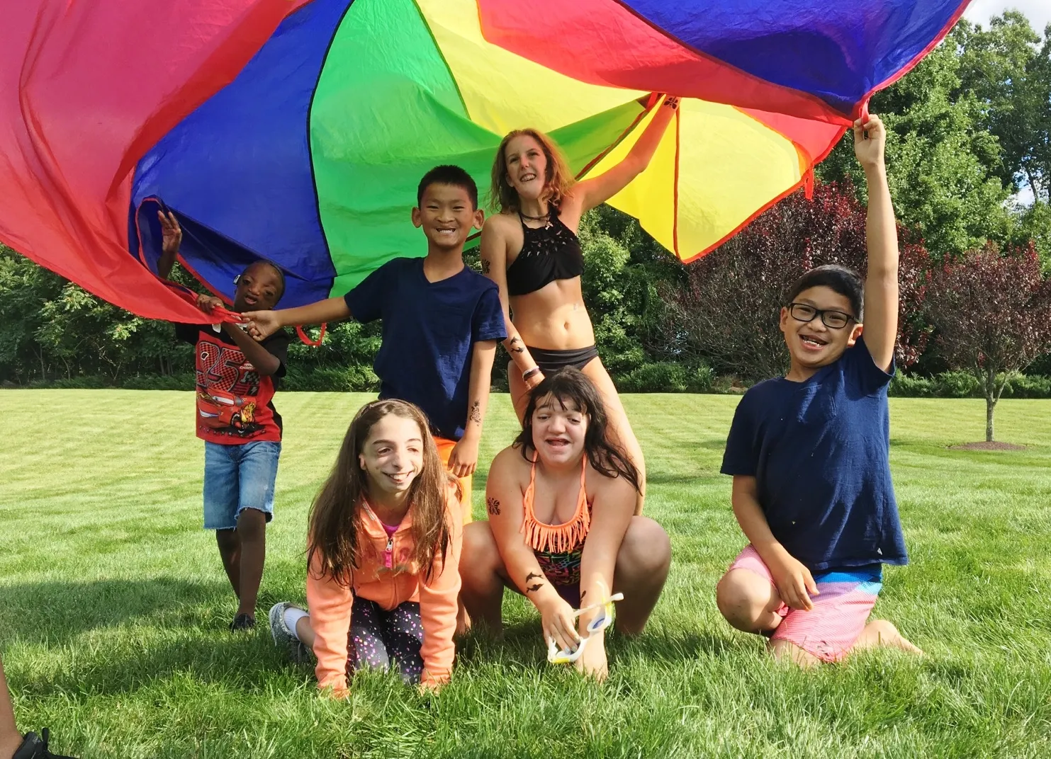 Children and adults play with a rainbow parachute outdoors