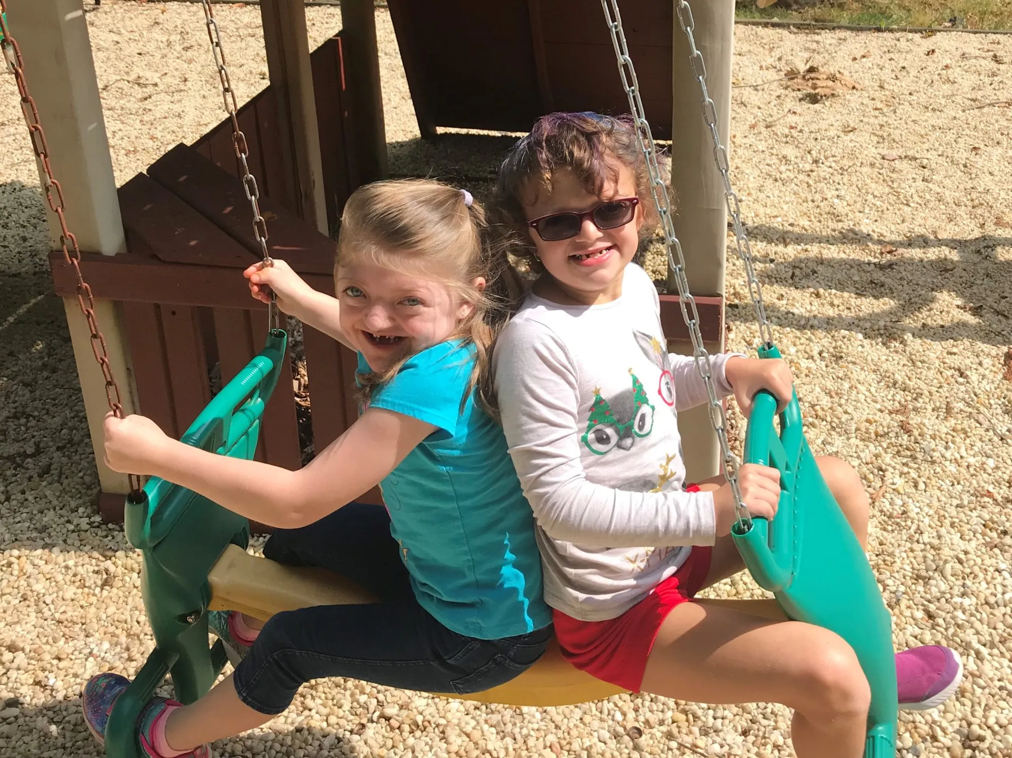 Two children swing together on playground equipment