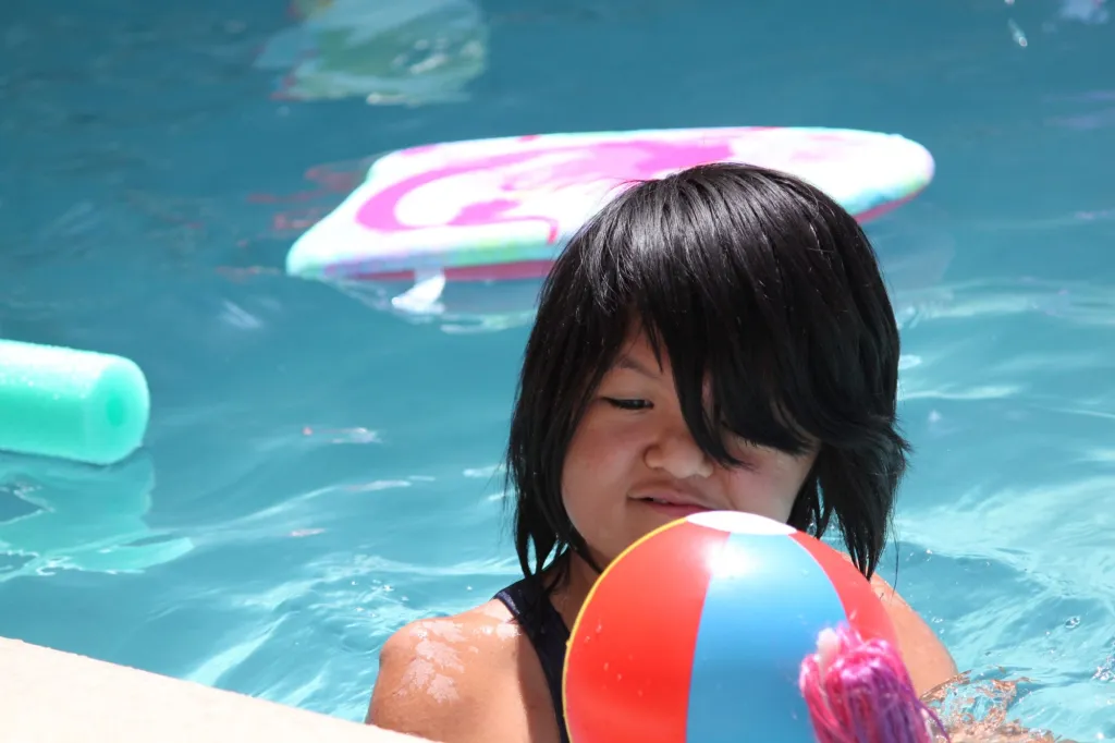 A child holds a colorful ball while swimming