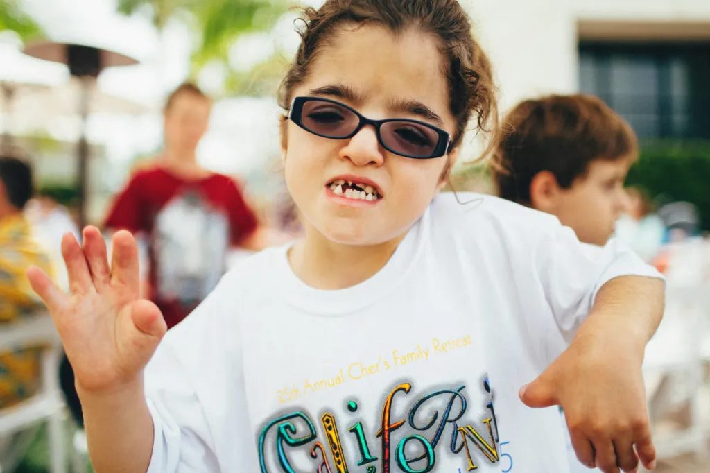A child wearing sunglasses and a CCA t-shirt smiles outdoors