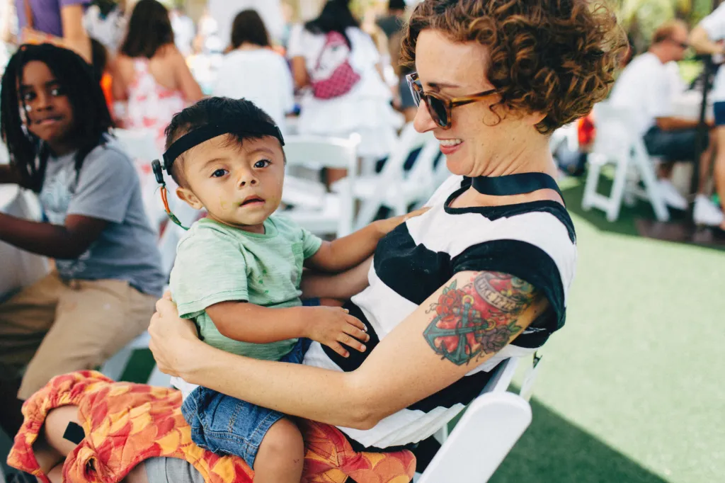 A parent holds a baby at an outdoor CCA family event
