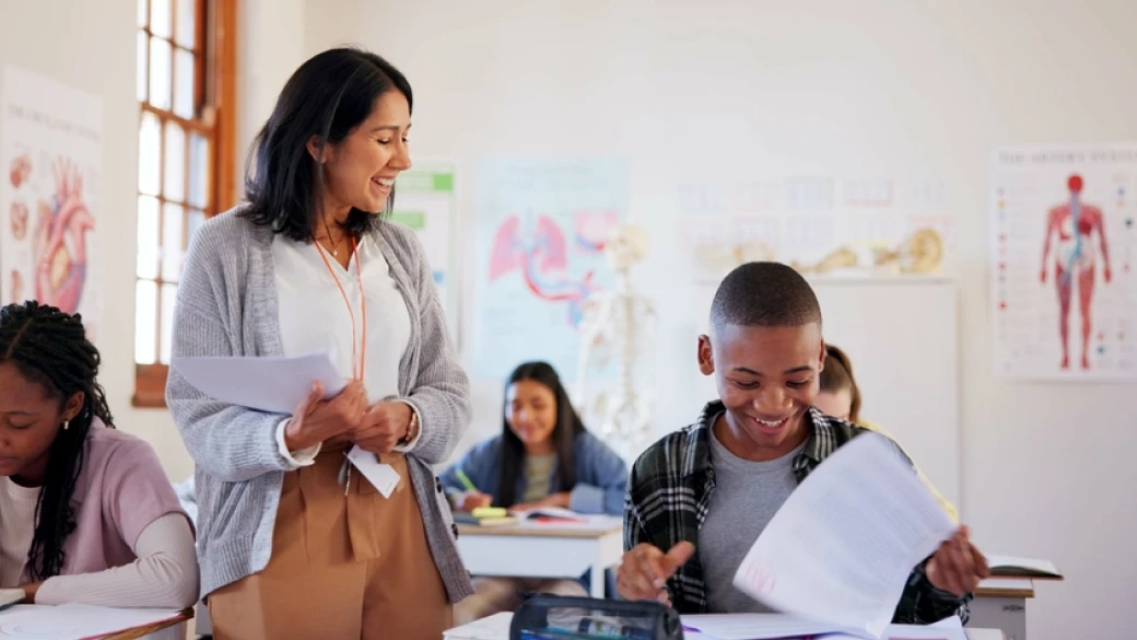 Teacher smiling at a student in a classroom with anatomy posters and students studying.